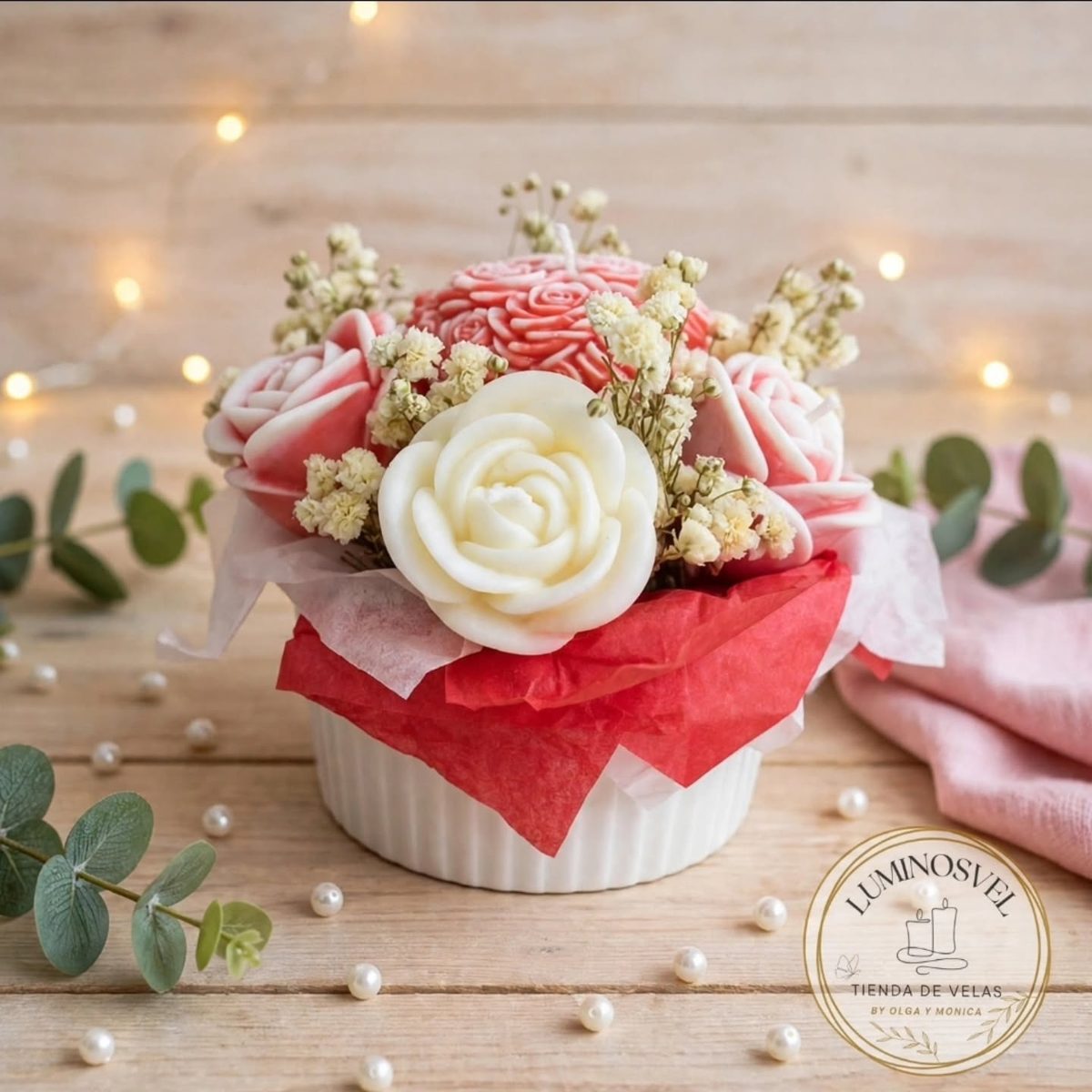 Maceta blanca con rosas de cera rojas, rosas y blancas sobre una mesa de madera con luces