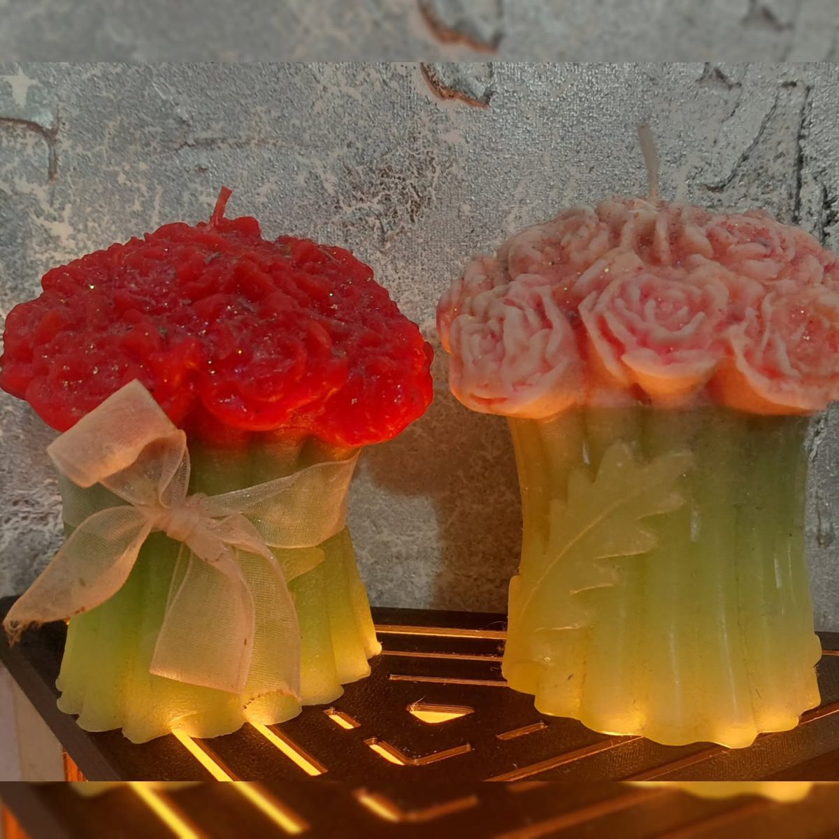 Dos ramos de rosas de cera, uno rojo y otro naranja, atados con lazo